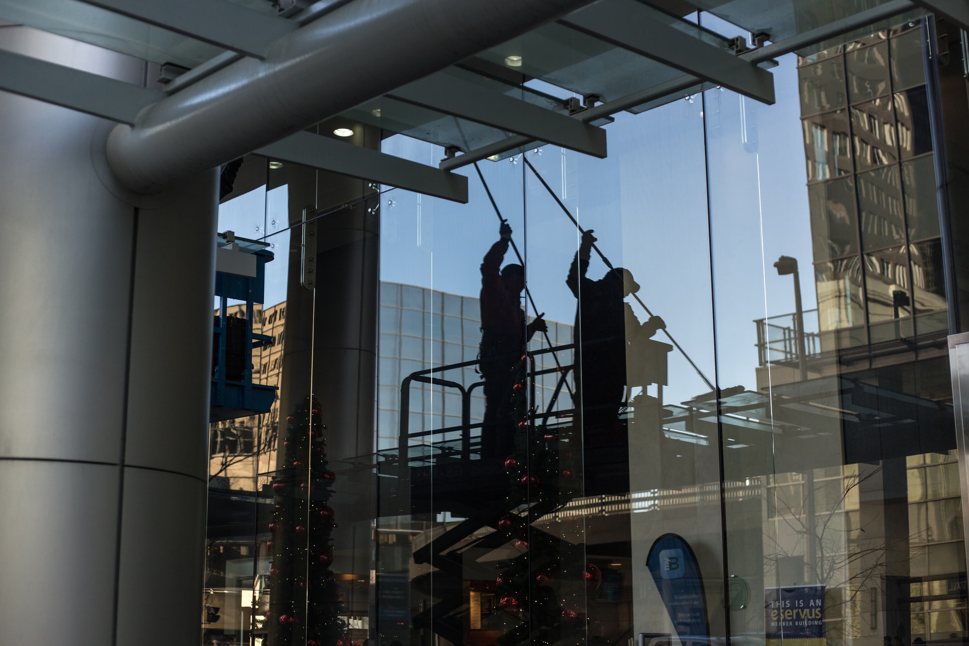 Glass-fronted urban building entrance with metal canopy and reflections of nearby structures.